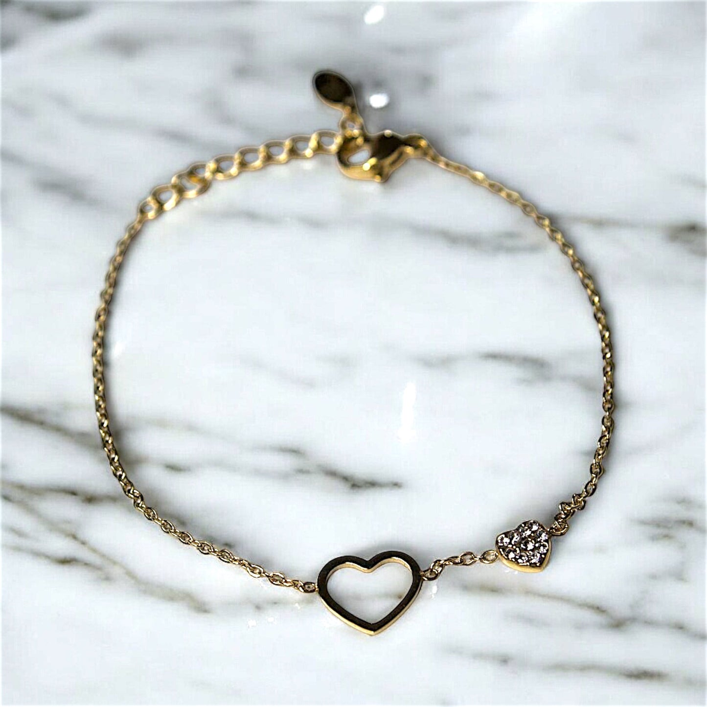 Elegant waterproof bracelet made of gold-plated stainless steel with open heart design and sparkling heart charm, displayed on a marble surface. Perfect for durable and stylish accessories